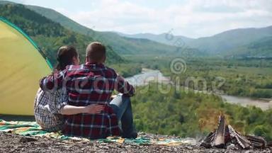 浪漫的旅游情侣在露营地拥抱，在青山的岩石山顶上篝火
